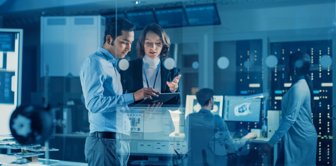 In Technology Research Facility: Female Project Manager Talks With Chief Engineer, they Consult Tablet Computer. Team of Industrial Engineers, Developers Work on Engine Design Using Computers